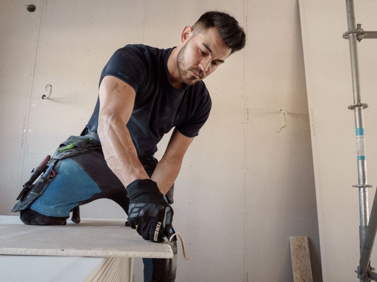 Handwerker richtet eine Gipsplatte vor einer bereits beplankten Wandfläche aus