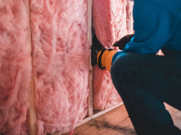 Mineralwolle liegt zwischen den Ständern einer offenen Wand, eine Dose sitzt bereits im Hohlraum